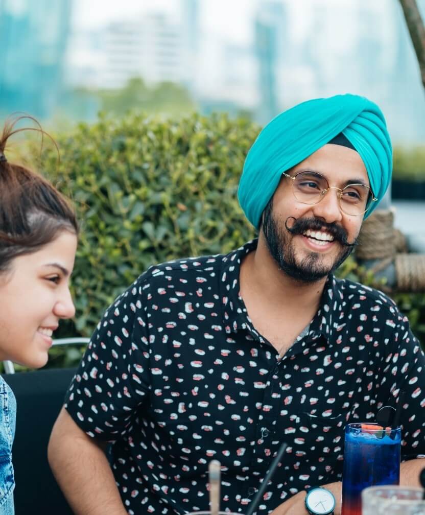 Two people smiling, seated, the man wears a light green turban.