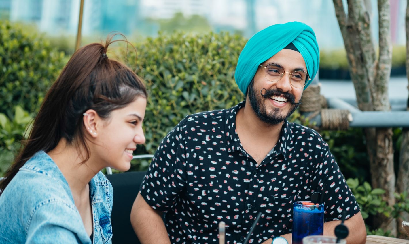 Two people smiling, seated, the man wears a light green turban.