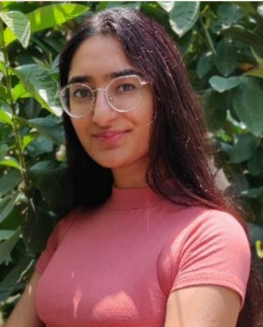 Woman smiling slightly for the photo, she has long hair, wears a pink polo shirt and glasses.